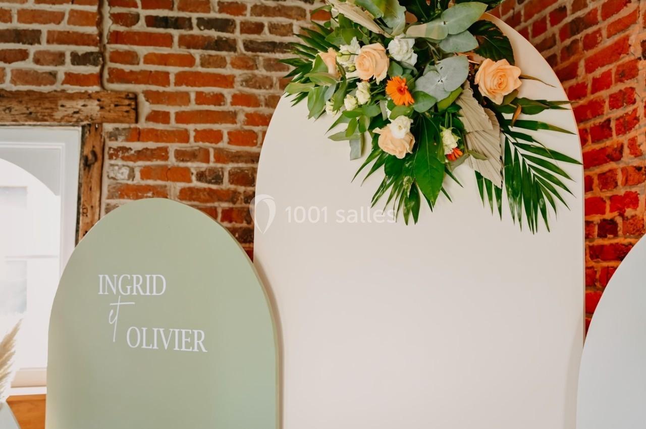 Décor floral avec roses et feuillage sur une arche blanche, à côté d'une autre arche verte portant des prénoms.