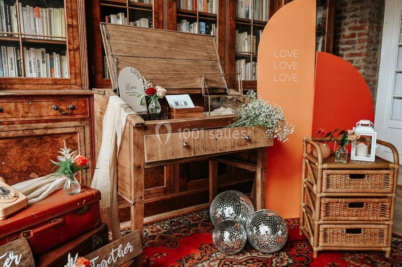 Meuble en bois avec machine à écrire, décoré de fleurs, miroirs boule et panneaux colorés dans une pièce avec bibliothèque.
