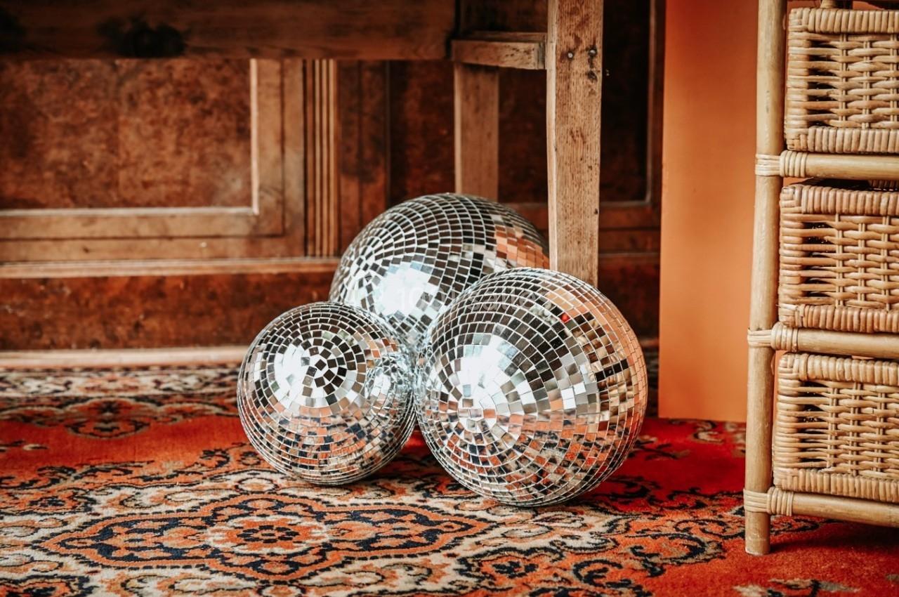Trois boules à facettes posées sur un tapis à motifs, près d'un meuble en bois et d'un panier en osier.
