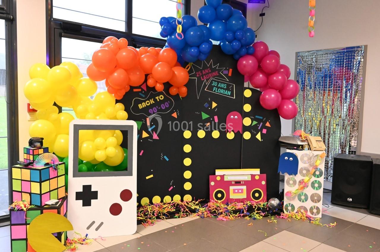 Décoration colorée sur le thème des années 90 avec ballons, Pac-Man, Game Boy et objets rétro dans une salle festive.