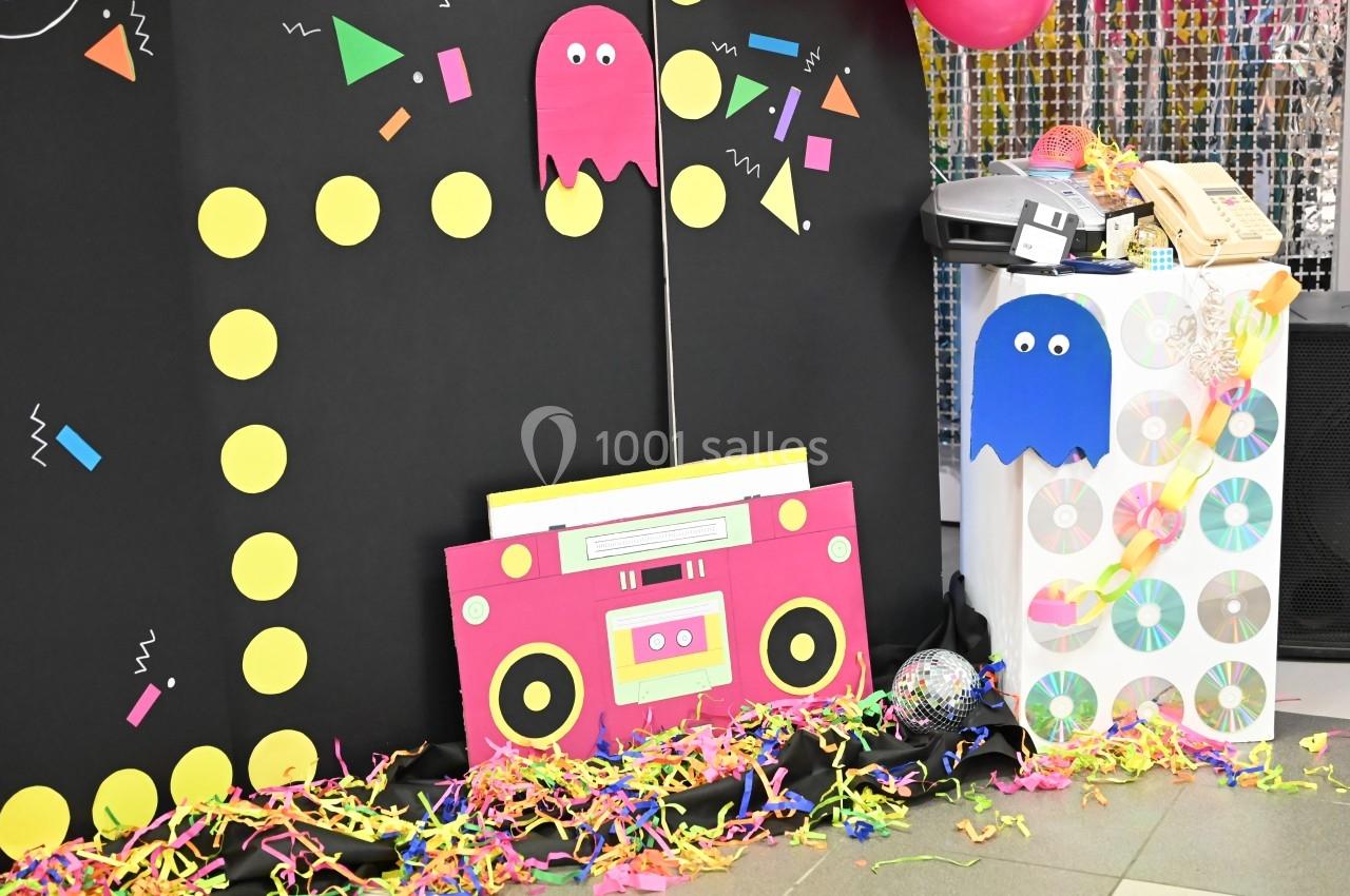 Décor festif inspiré des années 80 avec des éléments de Pac-Man, un poste radio rose et des CD colorés.