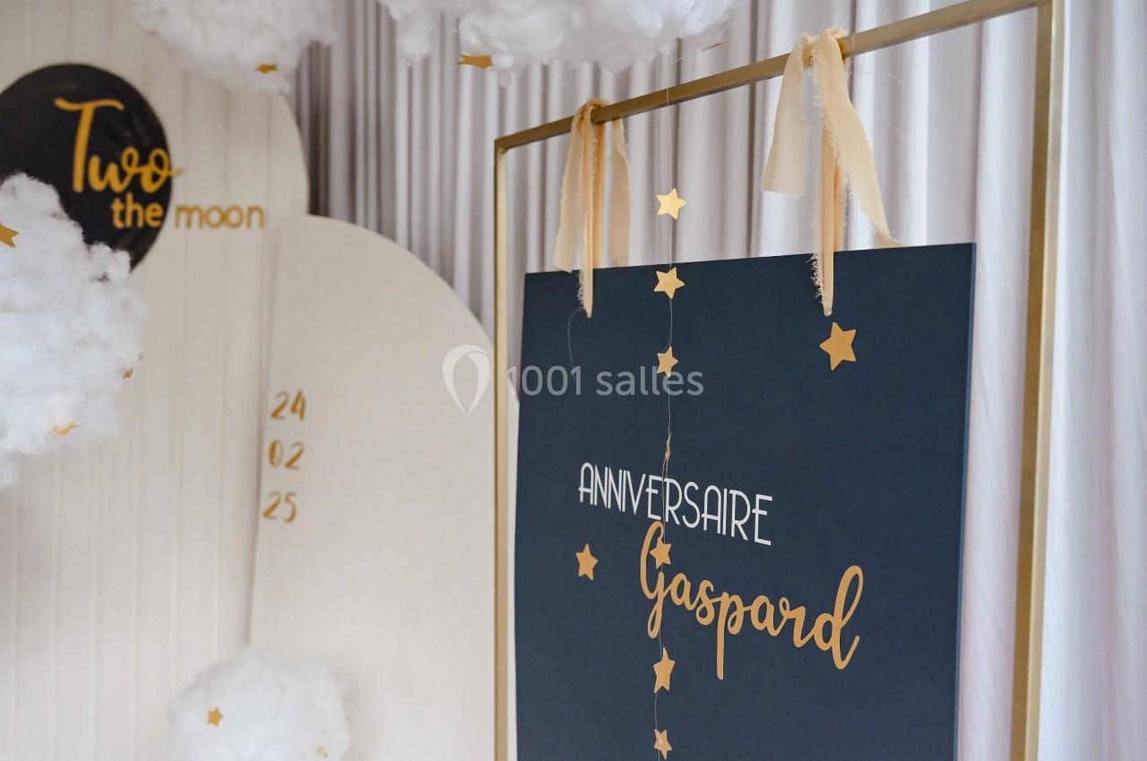 Décoration d'anniversaire avec un panneau noir ’Anniversaire Gaspard’, étoiles dorées et nuages suspendus.