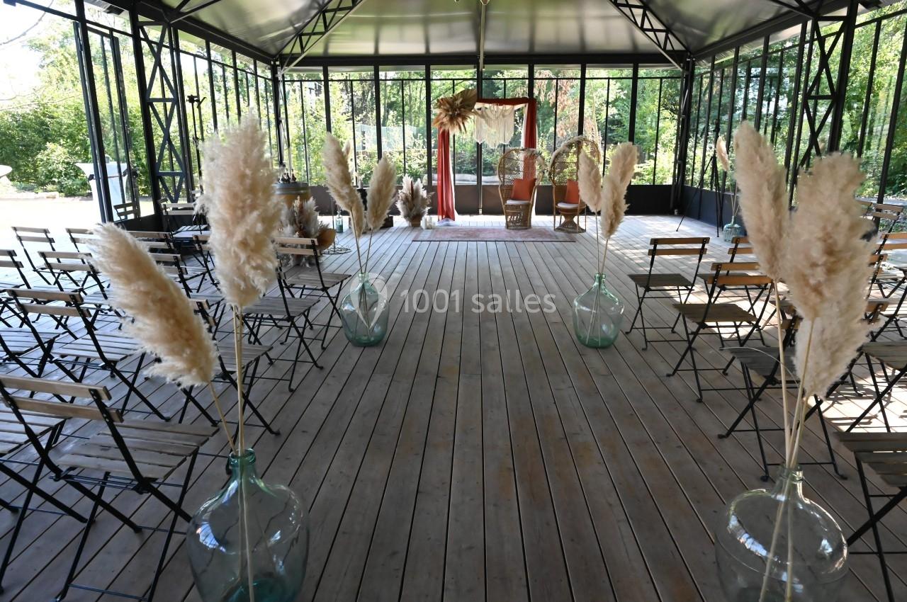 Salle de cérémonie en bois avec chaises pliantes, décorée de vases contenant des herbes de la pampa.