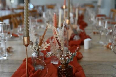 Table décorée avec des bougies torsadées, fleurs séchées et chemin de table rouge dans un cadre chaleureux.