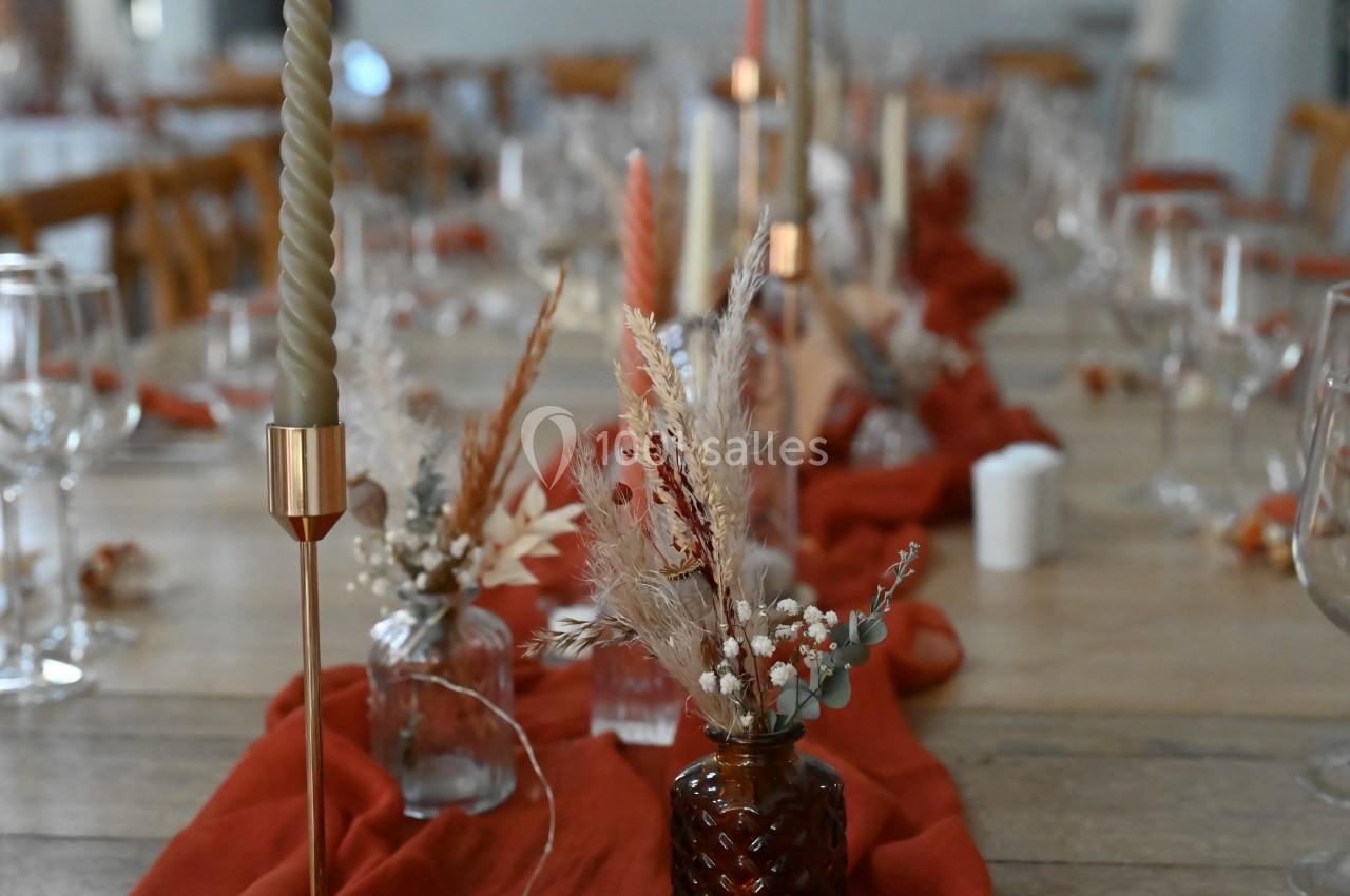 Table décorée avec des bougies torsadées, fleurs séchées et chemin de table rouge dans un cadre chaleureux.