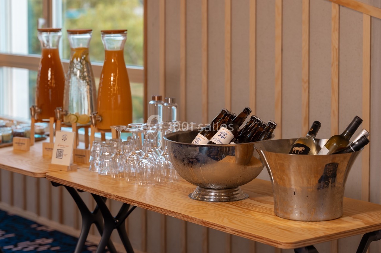 Buffet avec carafes de jus, verres, bouteilles de bière et de vin disposés sur une table en bois.