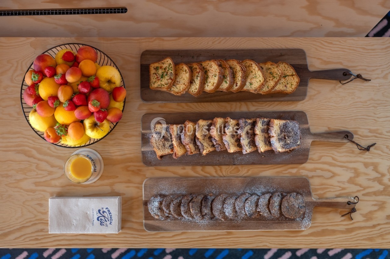 Plateau de fruits colorés, tranches de pain grillé, pâtisseries et biscuits disposés sur une table en bois clair.