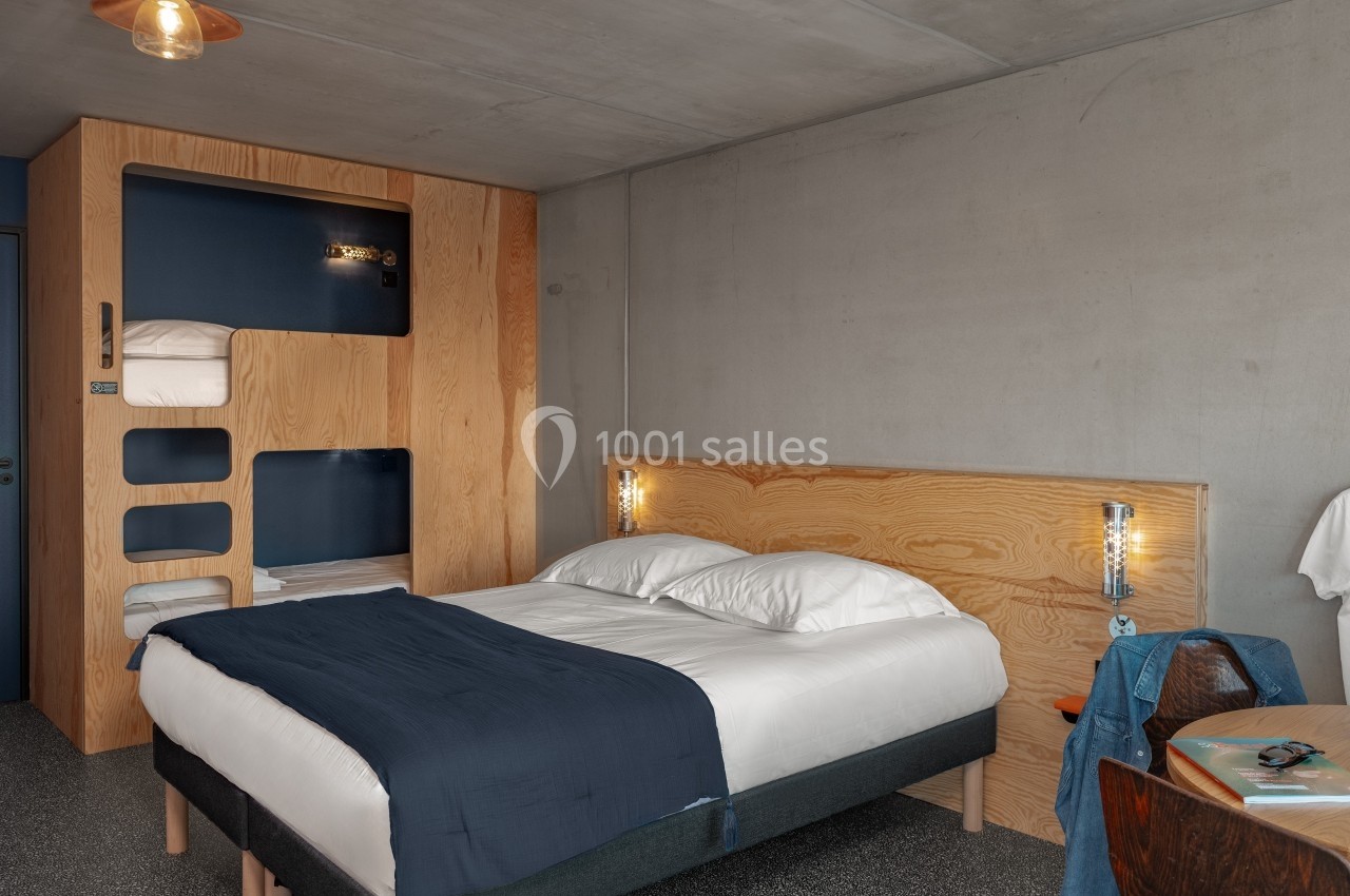 Chambre moderne avec lit double, literie blanche et bleue, mobilier en bois clair et éclairage minimaliste.