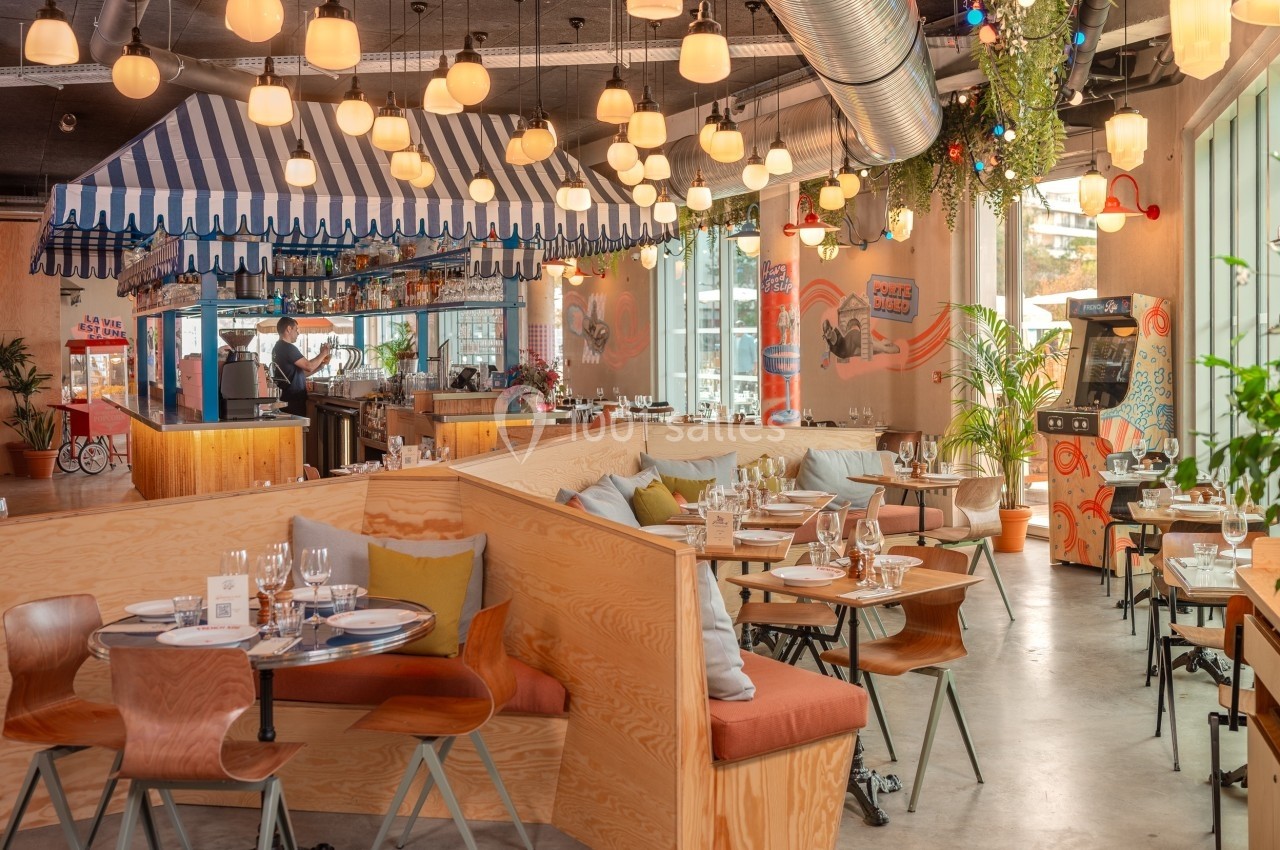 Salle de restaurant lumineuse avec tables en bois, banquettes colorées et décoration moderne et végétale.