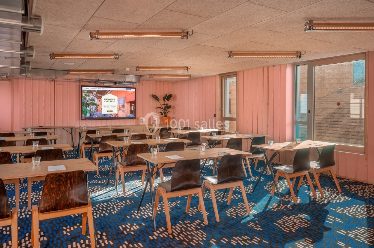 Salle de réunion lumineuse avec des tables en bois, des chaises modernes et un écran de présentation au fond.