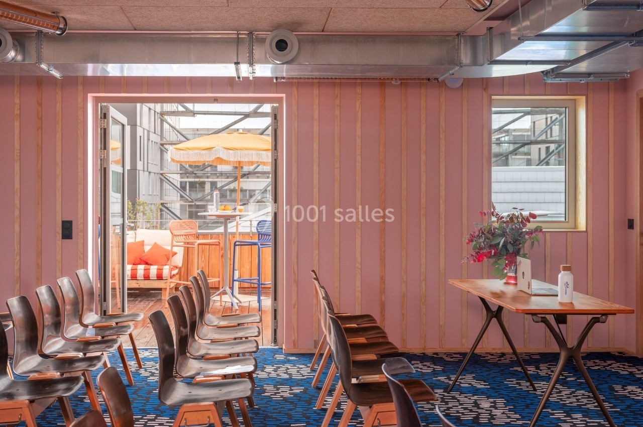 Salle de réunion avec des chaises alignées, une table en bois et une terrasse extérieure visible à travers une porte ouverte.