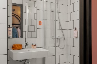 Salle de bain moderne avec douche vitrée, carrelage blanc, lavabo suspendu et éclairage mural.