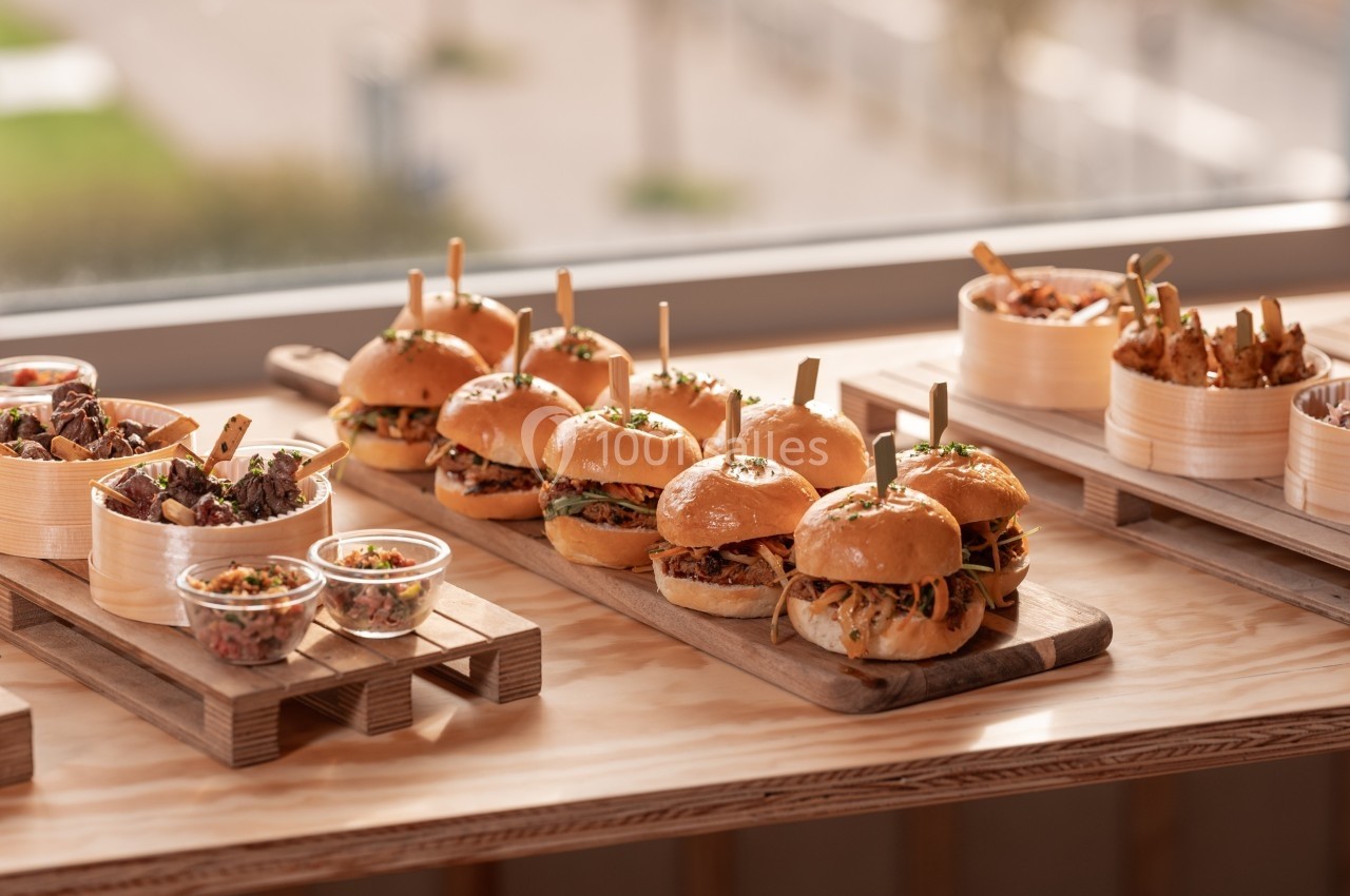 Plateau en bois avec burgers garnis, accompagnés de salades et de petites portions dans des bols en bambou.