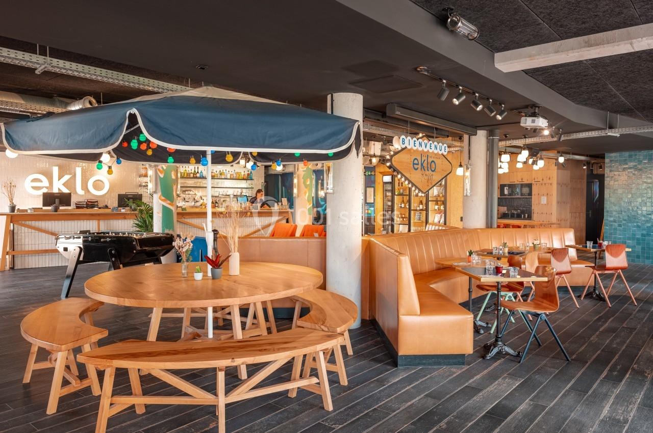 Espace de restauration moderne avec tables en bois, banquettes orange, éclairage chaleureux et décoration colorée.