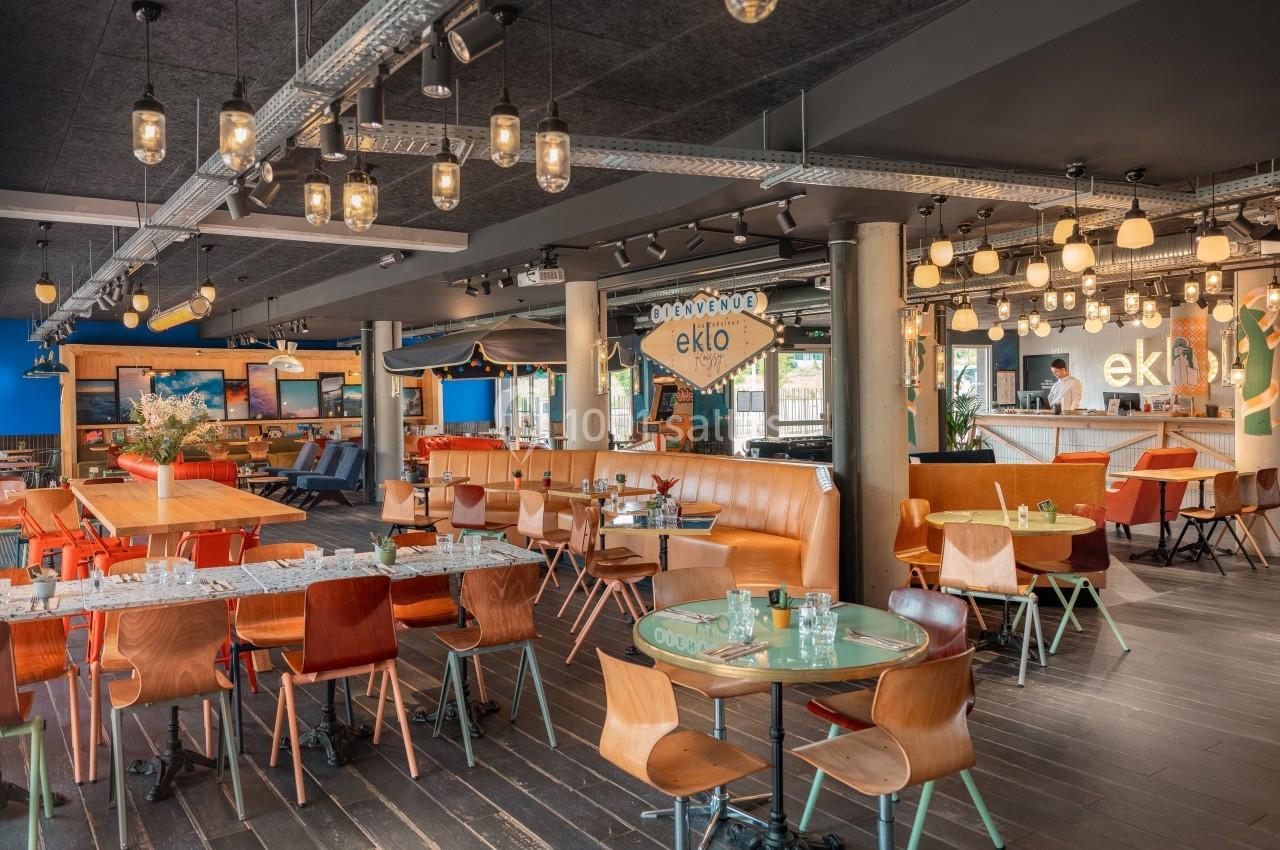 Salle de restaurant moderne avec tables en bois, banquettes orange et éclairage suspendu.