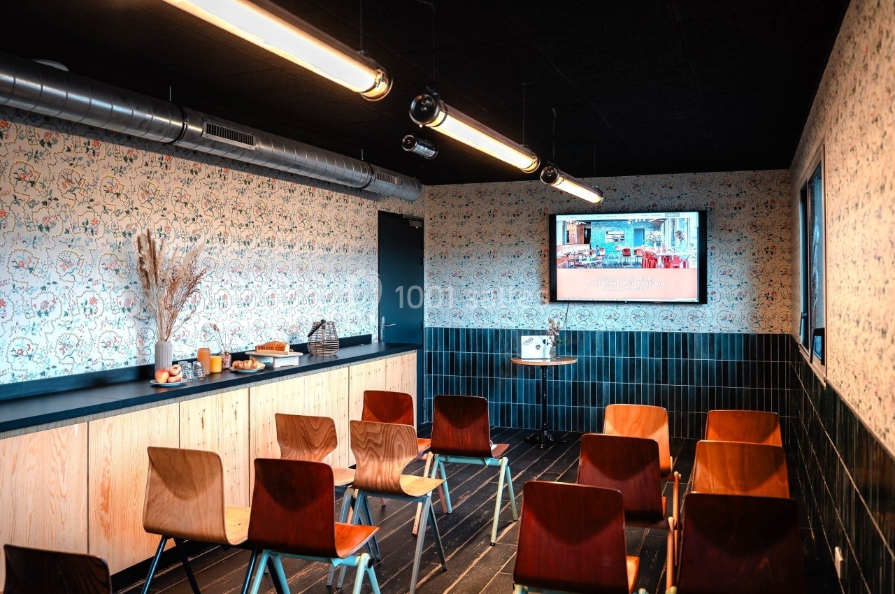 Salle de réunion équipée de chaises en bois, écran mural, buffet avec collations et décoration murale colorée.