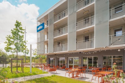 Chambre moderne avec lits superposés en bois, table ronde, chaise, et porte donnant sur l'extérieur.