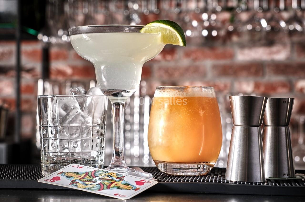 Deux cocktails sur un bar, un margarita avec une tranche de citron vert et un verre orange, entourés de glaçons et…