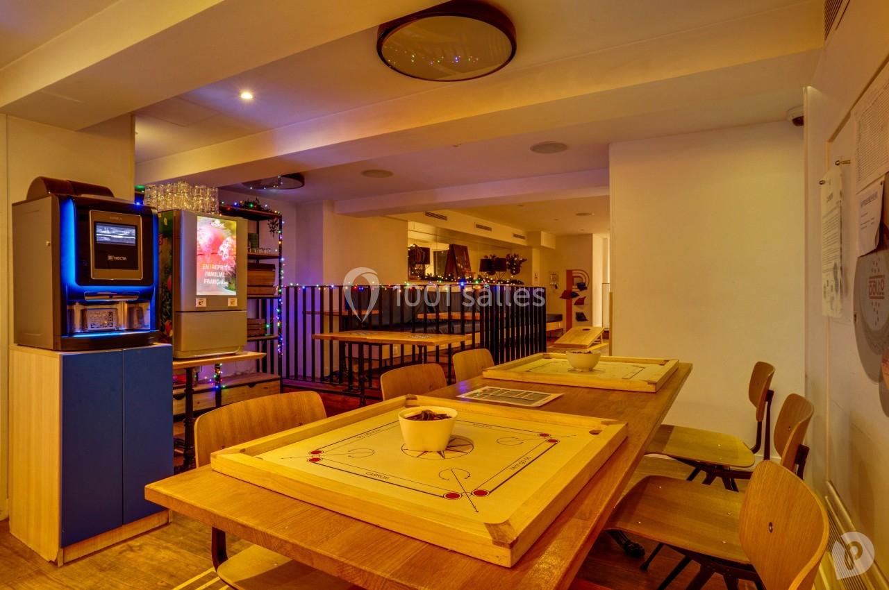 Salle conviviale avec tables en bois, jeux de société, distributeur automatique et décorations lumineuses.