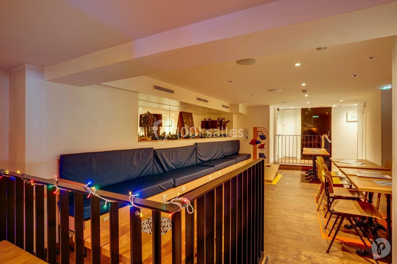 Espace intérieur chaleureux avec canapé bleu, tables en bois, chaises et guirlandes lumineuses colorées.