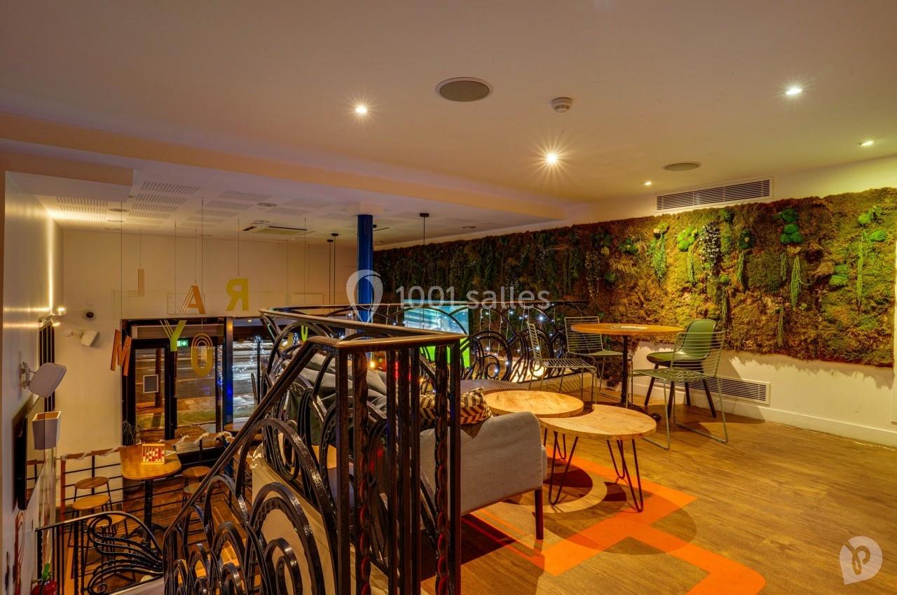 Espace intérieur moderne avec murs végétalisés, mobilier en bois et métal, éclairage chaleureux et mezzanine.