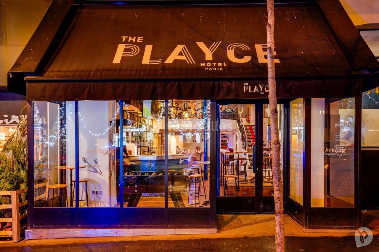 Façade vitrée d'un hôtel avec terrasse extérieure, éclairage nocturne et enseigne ’The Playce Hotel Paris’.