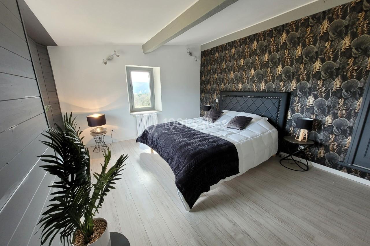 Chambre lumineuse avec lit double, mur à motif végétal, lampe de chevet et plante décorative au sol.