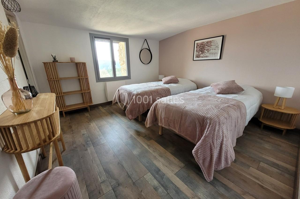 Chambre lumineuse avec deux lits simples, décoration épurée, mobilier en bois et linge de lit rose.