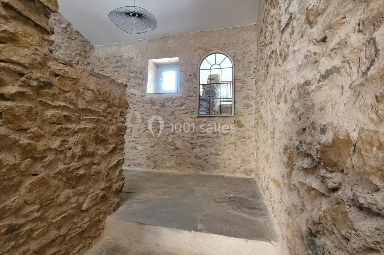 Mur en pierre apparente avec une fenêtre rectangulaire et une fenêtre cintrée, éclairées par la lumière naturelle.