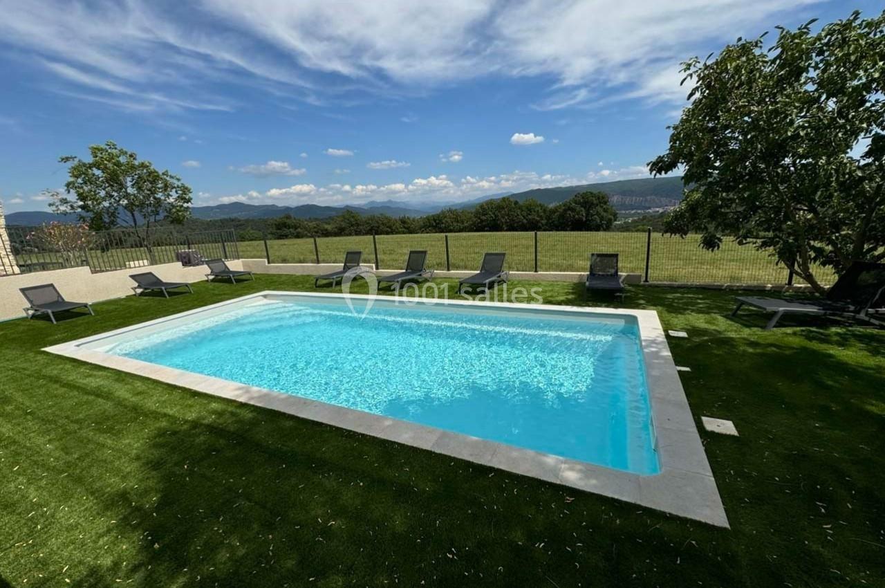 Piscine rectangulaire entourée de transats sur une pelouse, avec vue sur un paysage vallonné et ciel dégagé.