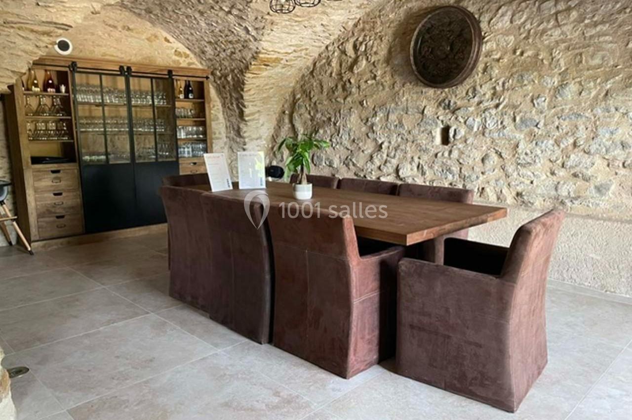 Salle à manger avec table en bois, chaises marron, murs en pierre apparente et meuble vitré contenant de la vaisselle.