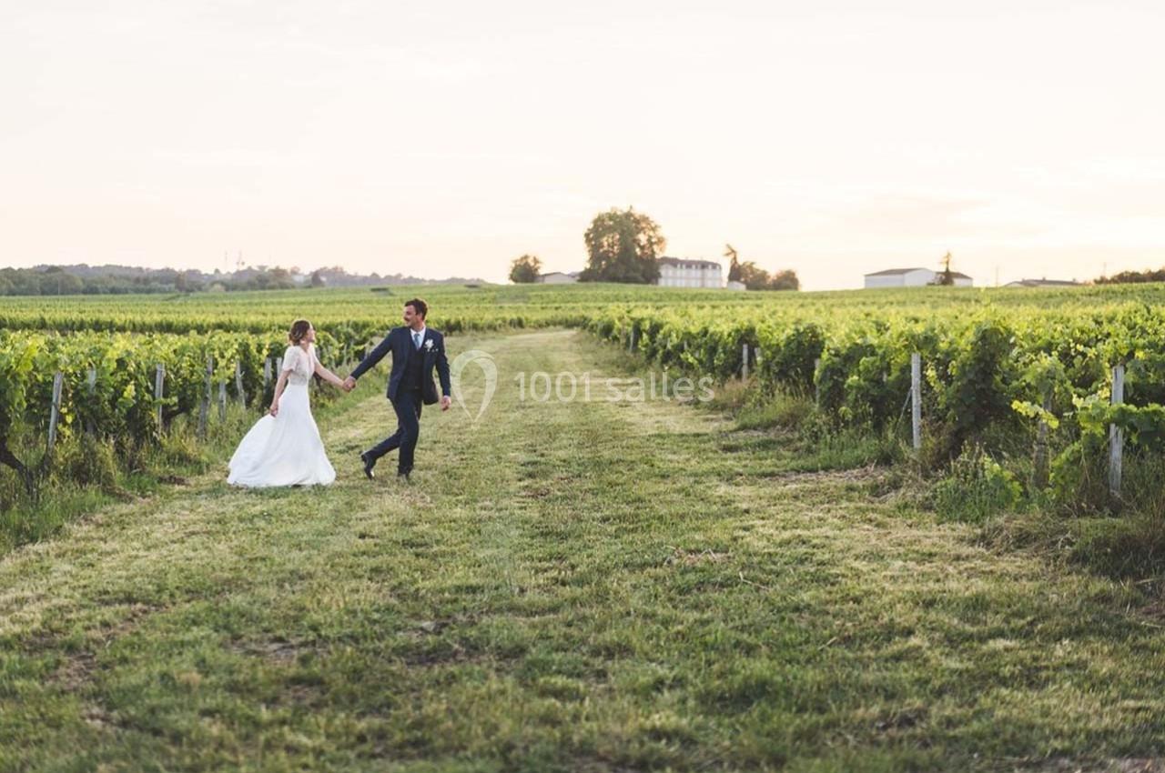 Un couple en tenue de mariage marche main dans la main au milieu d'un vignoble au coucher du soleil.