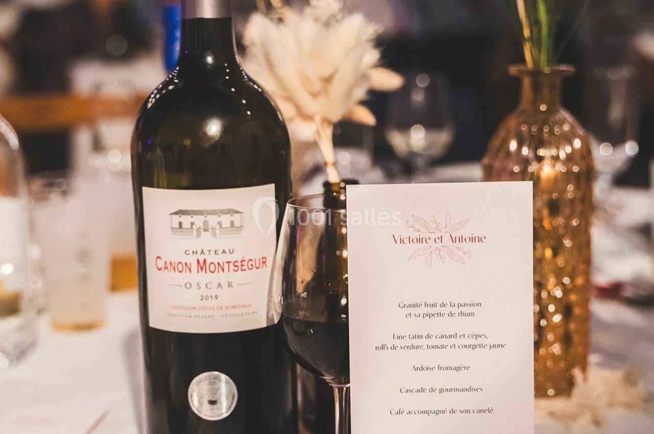 Bouteille de vin rouge Château Canon Montsegur posée sur une table dressée avec un verre et un menu imprimé.