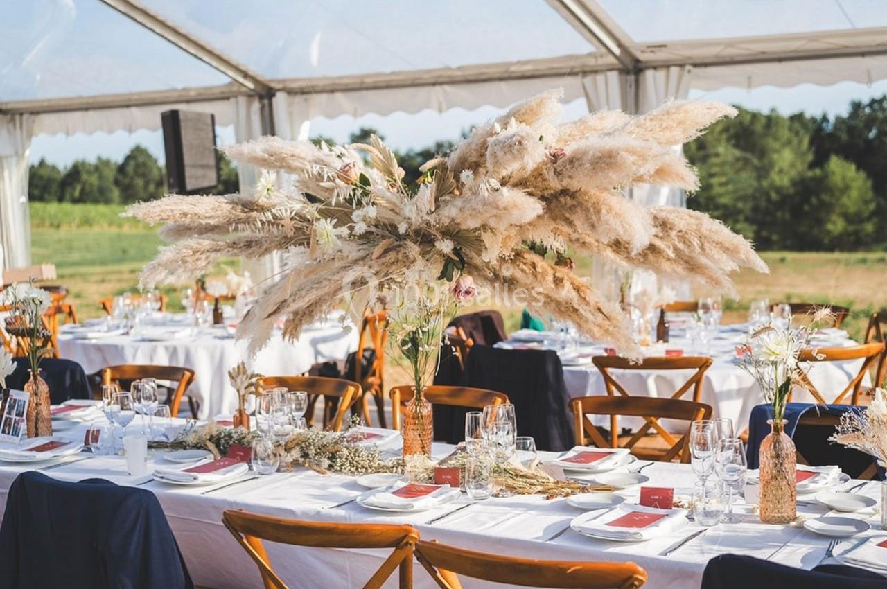 Grande table de réception décorée avec des fleurs séchées et des herbes de la pampa sous une tente transparente.