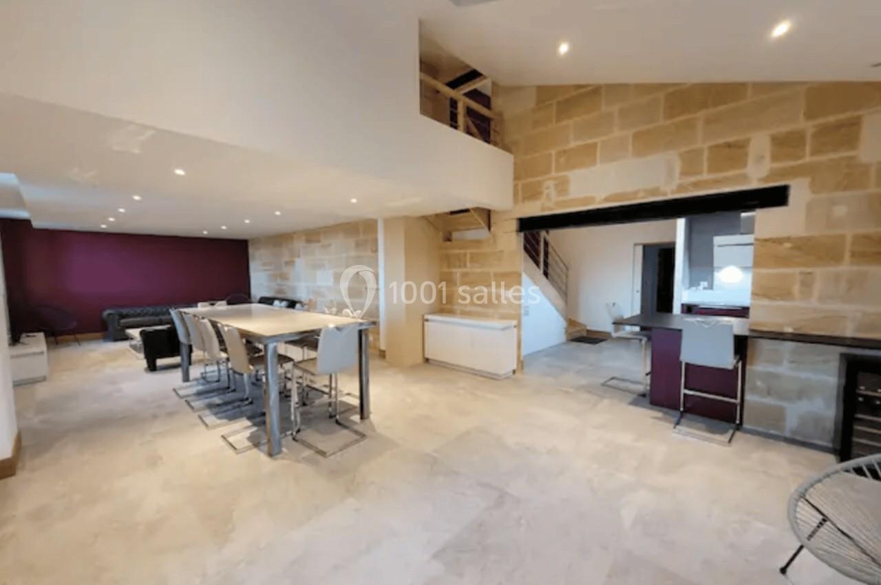 Salle à manger spacieuse avec table et chaises modernes, murs en pierre apparente et escalier menant à l'étage.