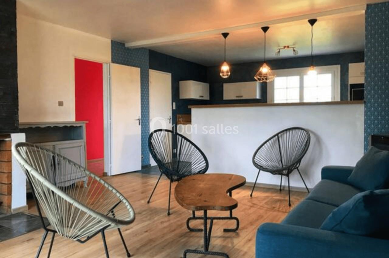 Salon moderne avec parquet, murs bleus, canapé bleu, chaises design en métal et bois, et suspensions lumineuses.