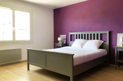 Lit avec tête de lit en métal blanc, draps et oreillers blancs, lampe de chevet sur une table contre un mur vert.