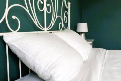 Lit avec tête de lit en métal blanc, draps et oreillers blancs, lampe de chevet sur une table contre un mur vert.