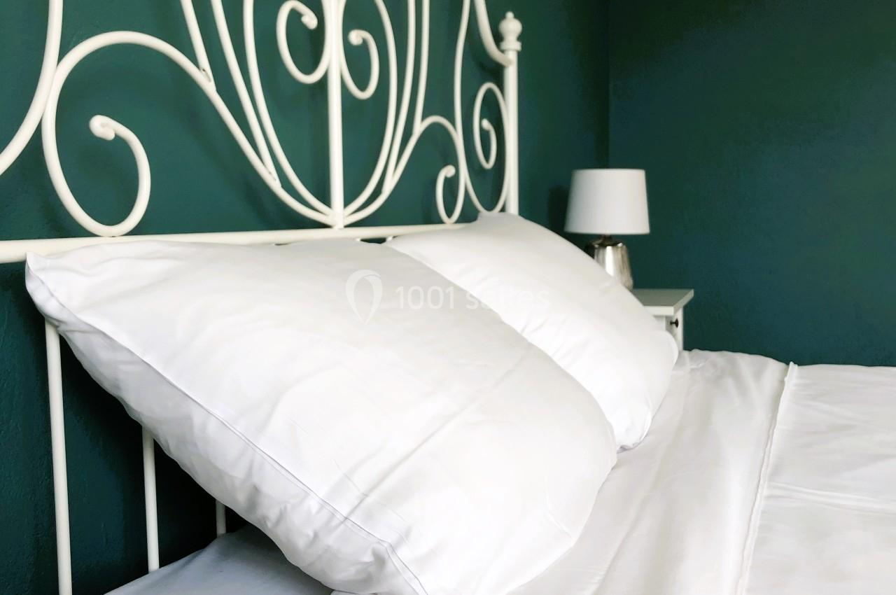 Lit avec tête de lit en métal blanc, draps et oreillers blancs, lampe de chevet sur une table contre un mur vert.