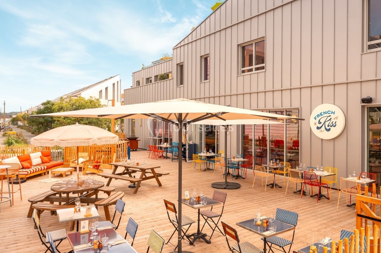 Terrasse ensoleillée avec tables, chaises colorées et parasols devant un bâtiment moderne.
