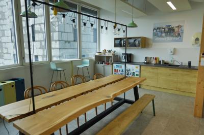 Deux fauteuils noirs et une table jaune sur une terrasse en bois, près de baies vitrées et de stores.