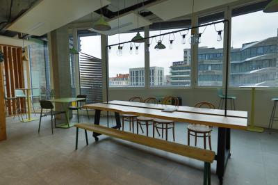 Deux fauteuils noirs et une table jaune sur une terrasse en bois, près de baies vitrées et de stores.