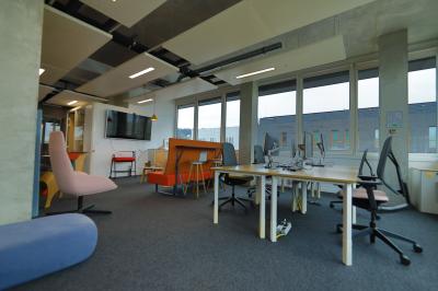 Deux fauteuils noirs et une table jaune sur une terrasse en bois, près de baies vitrées et de stores.