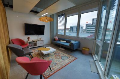 Deux fauteuils noirs et une table jaune sur une terrasse en bois, près de baies vitrées et de stores.