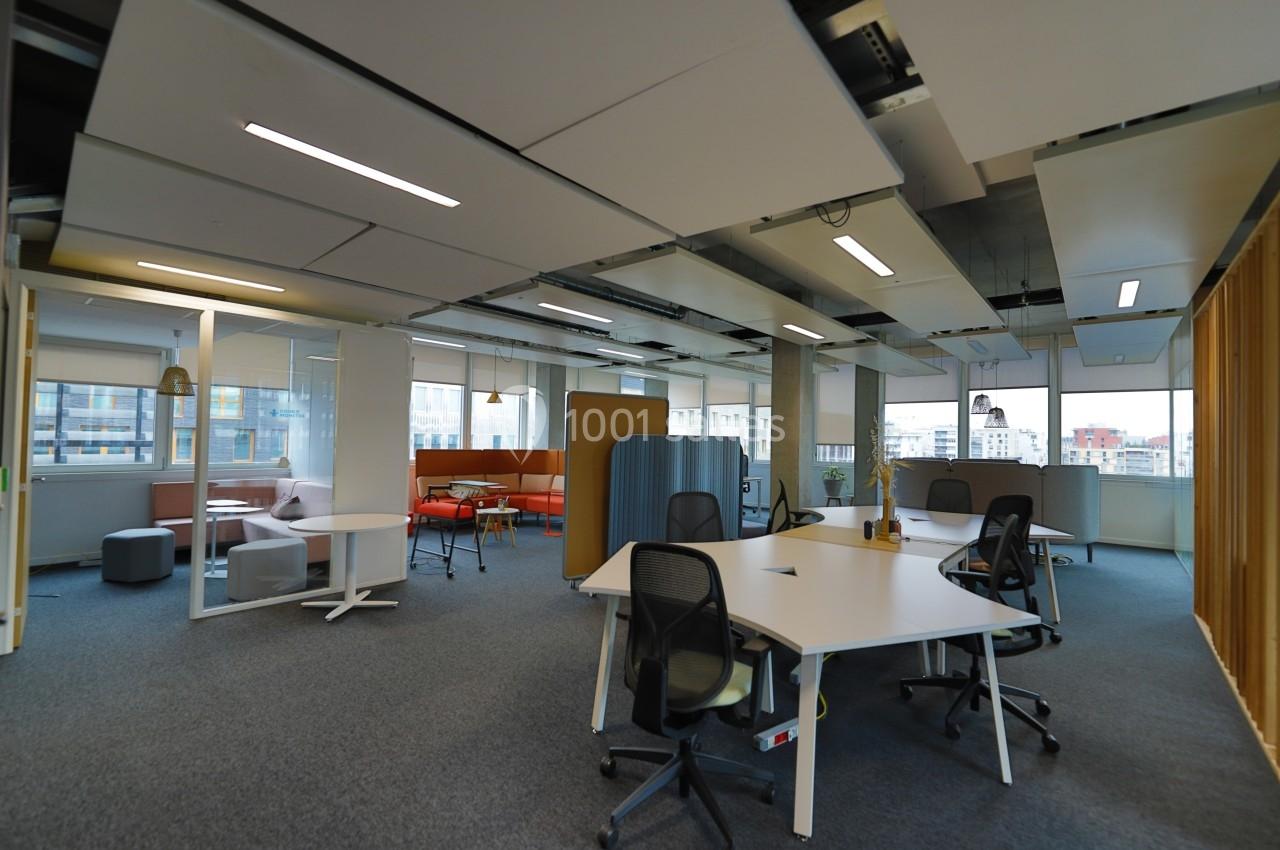 Espace de travail moderne avec bureaux blancs, chaises ergonomiques et zones de détente dans un environnement lumineux.