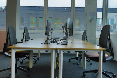Deux fauteuils noirs et une table jaune sur une terrasse en bois, près de baies vitrées et de stores.