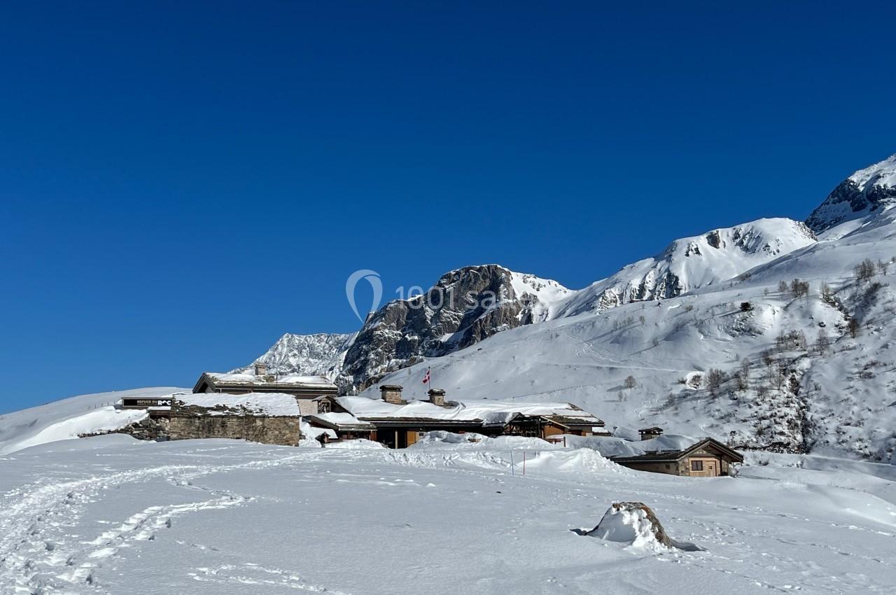 Chalets en bois entourés de neige au pied de montagnes sous un ciel bleu clair.