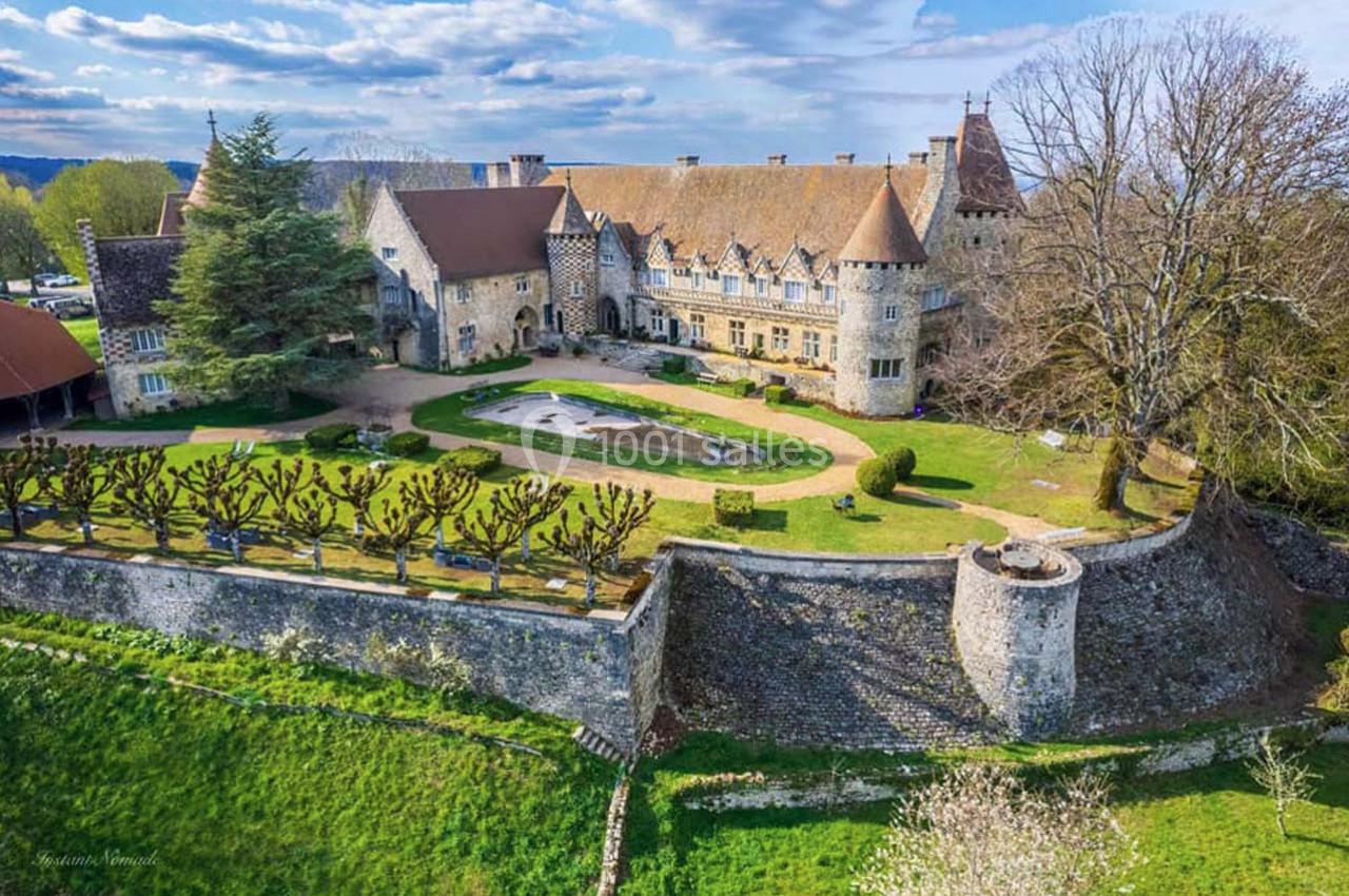 Vue aérienne d'un château historique entouré de jardins, d'arbres taillés et de murs en pierre.