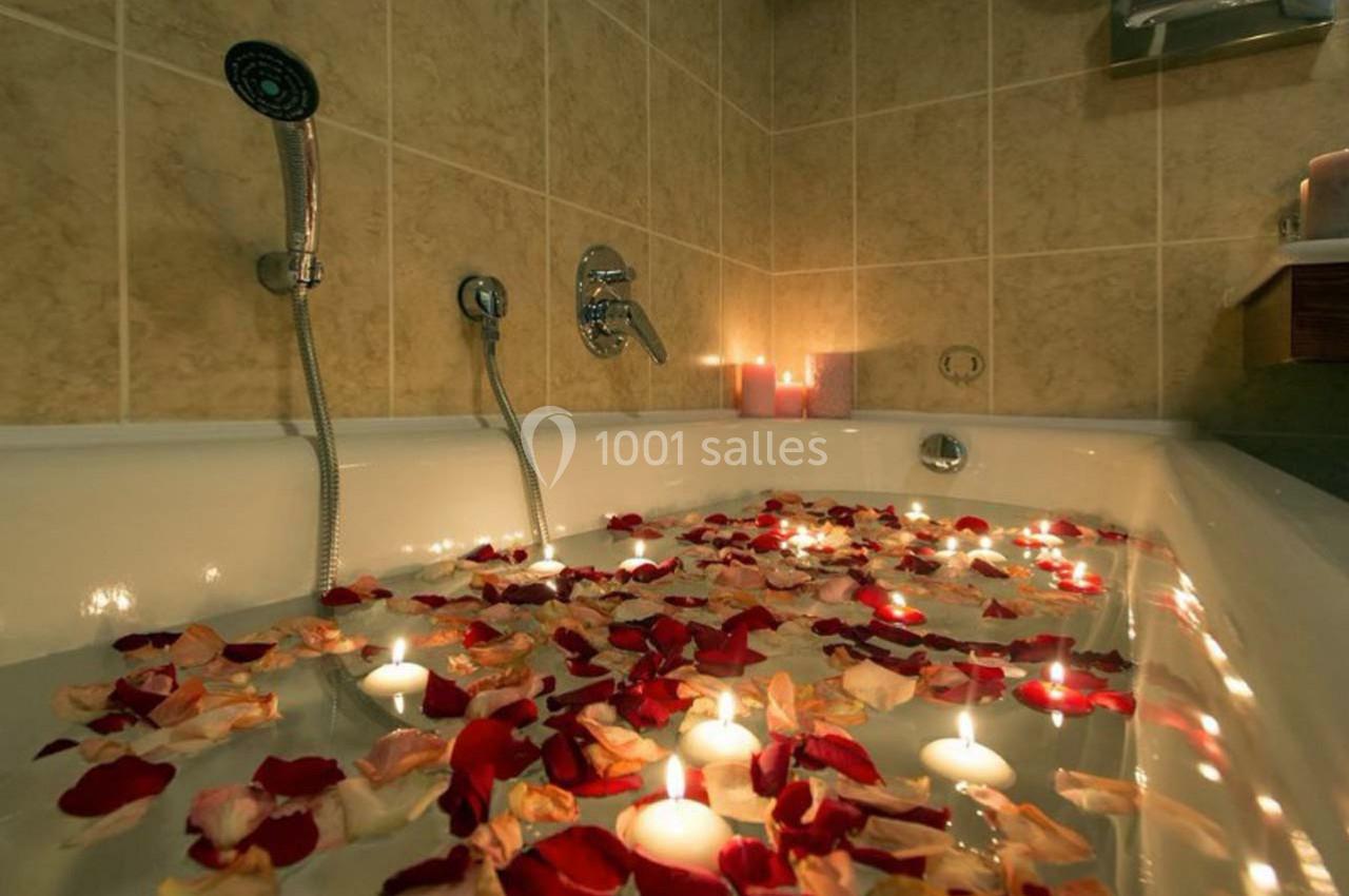 Baignoire remplie d'eau avec des pétales de rose et des bougies flottantes dans une salle de bain carrelée.