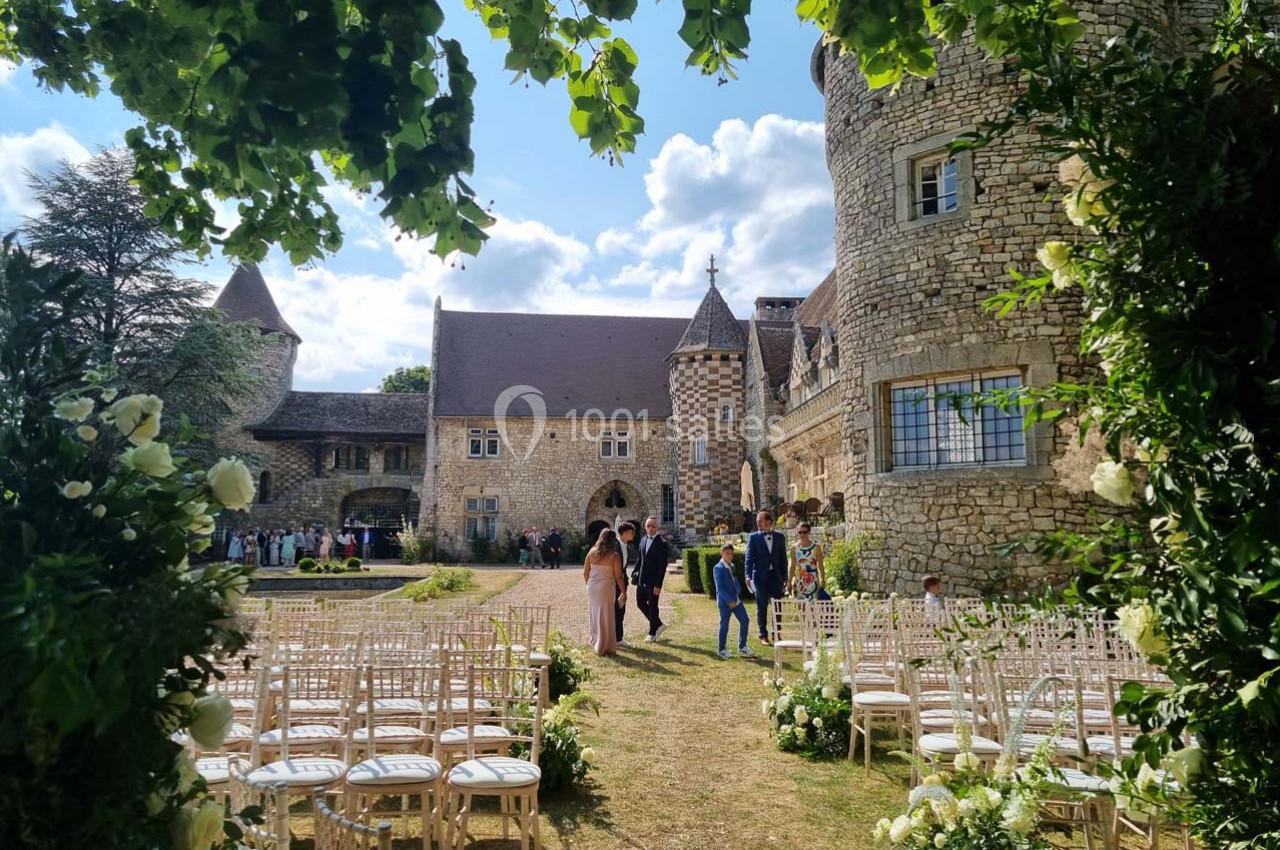 Cérémonie en plein air dans la cour d'un château en pierre, avec des chaises alignées et des invités en arrière-plan.